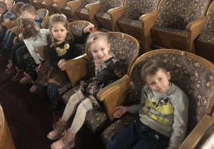 Dzieci siedzą w fotelach w teatrze.
